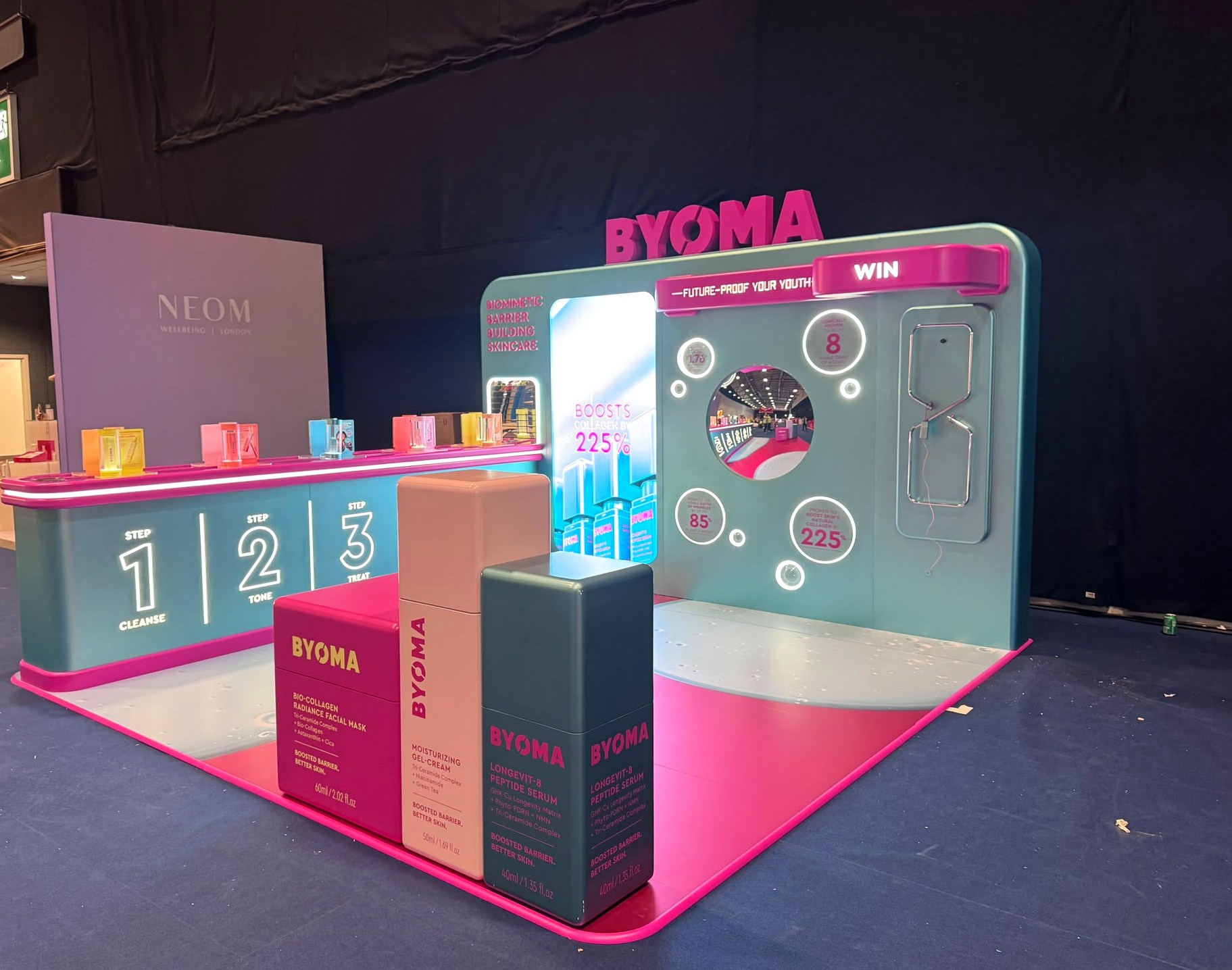 Angled view of BYOMA event installation with illuminated counters and branded product plinths